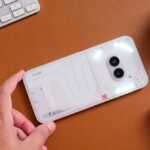 Biały smartfon z podwójnym aparatem fotograficznym na pomarańczowym stole biurowym.