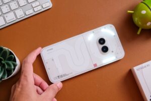 Biały smartfon z podwójnym aparatem fotograficznym na pomarańczowym stole biurowym.